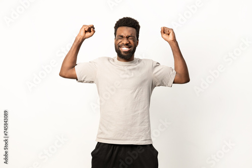 An ecstatic African American man raises his arms in victory, exuding happiness and success on a white backdrop.
