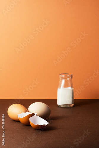 Three eggs with milk in glass bottle on brown background photo