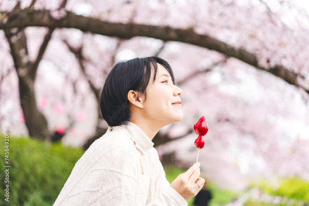 Side view asian woman eating japanese style street food strawberry candy japan tasty travel with sakura tree background Side view asian woman eating japanese style street food strawberry candy japan tasty travel with sakura tree background