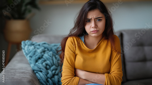 Young woman holding stomach with hands while sitting on the couch at home
