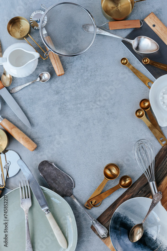 Various kitchen utensils are laid out in a circle on a gray concrete background. sieve, measuring spoons, knives, pizza cutter. space for text