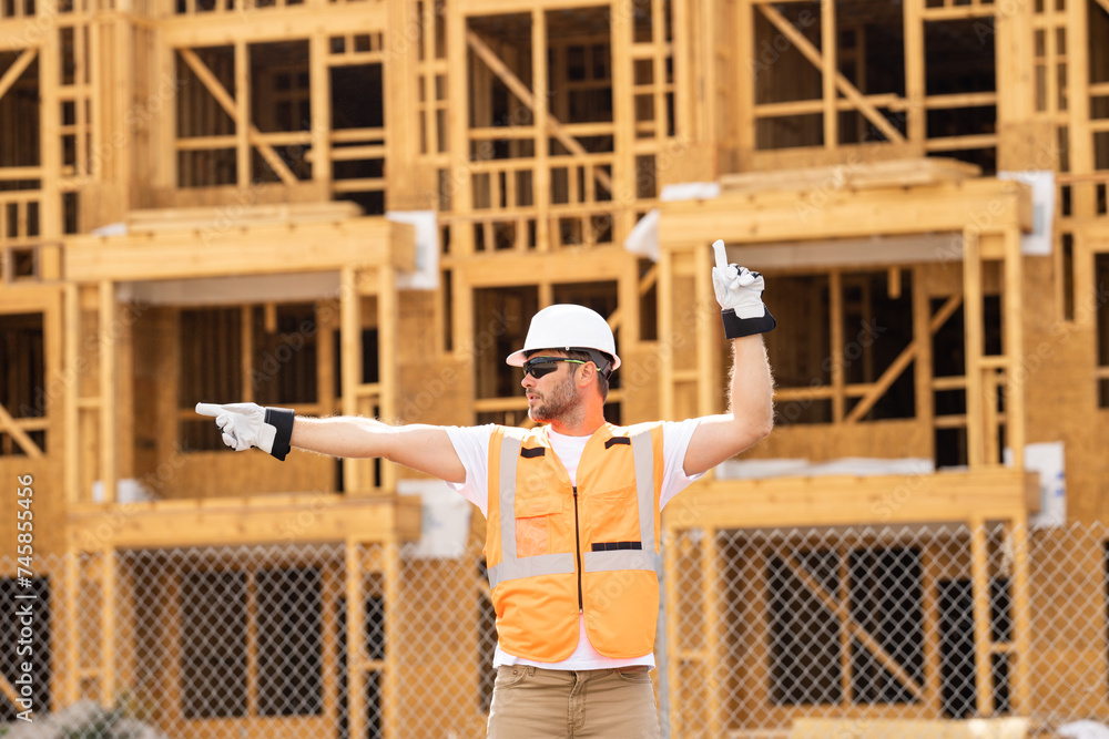 roofer builder working on roog structure of building on construction site. handsome young male builder in hard hat smiling at camera. Construction Worker on Duty. Contractor and the Wooden House Frame