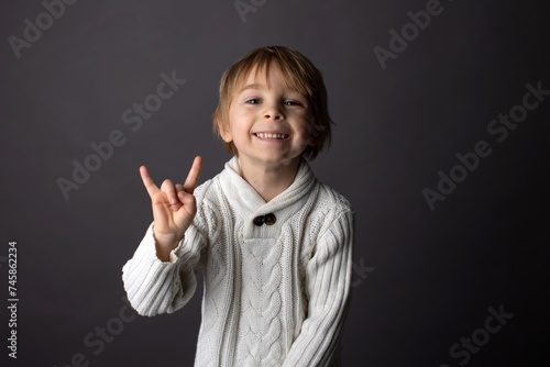 Cute little toddler boy, showing gesture in sign language on gray background, isolated image, child showing hand sings photo