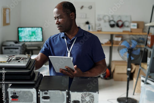 Experienced African American male technician with tablet checking broken hardware or some other equipment while consulting online manual