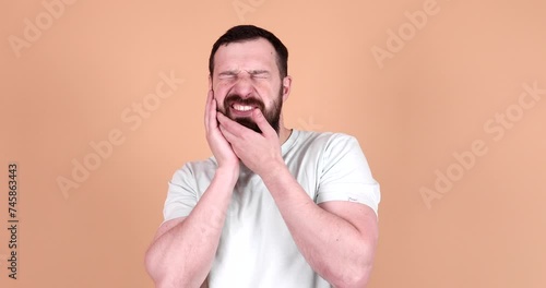 Young man wearing a t-shirt touching mouth with hand with painful expression because of toothache or dental illness on teeth over isolated beige background. photo