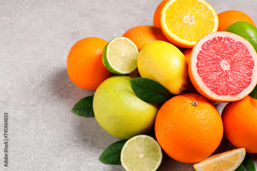 Pile of different fresh citrus fruits and leaves on grey textured table, closeup. Space for text © New Africa
