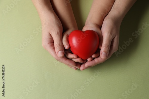 Mother and her child holding red decorative heart on light green background  top view. Space for text