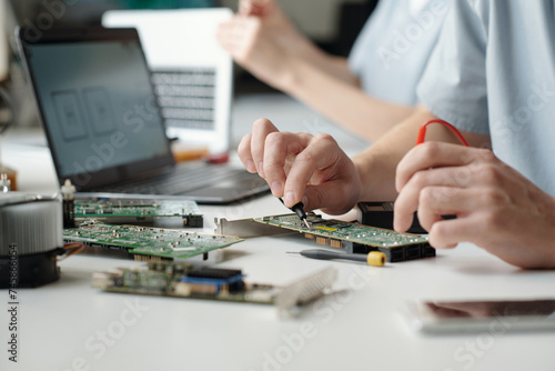 Hands of young male professional engineer of repair service center working with electric handtool while checking motherboard