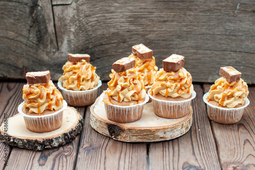 Delicious chocolate cupcakes with peanut butter frosting, chocolate bites and salted caramel sauce on rustic wooden background