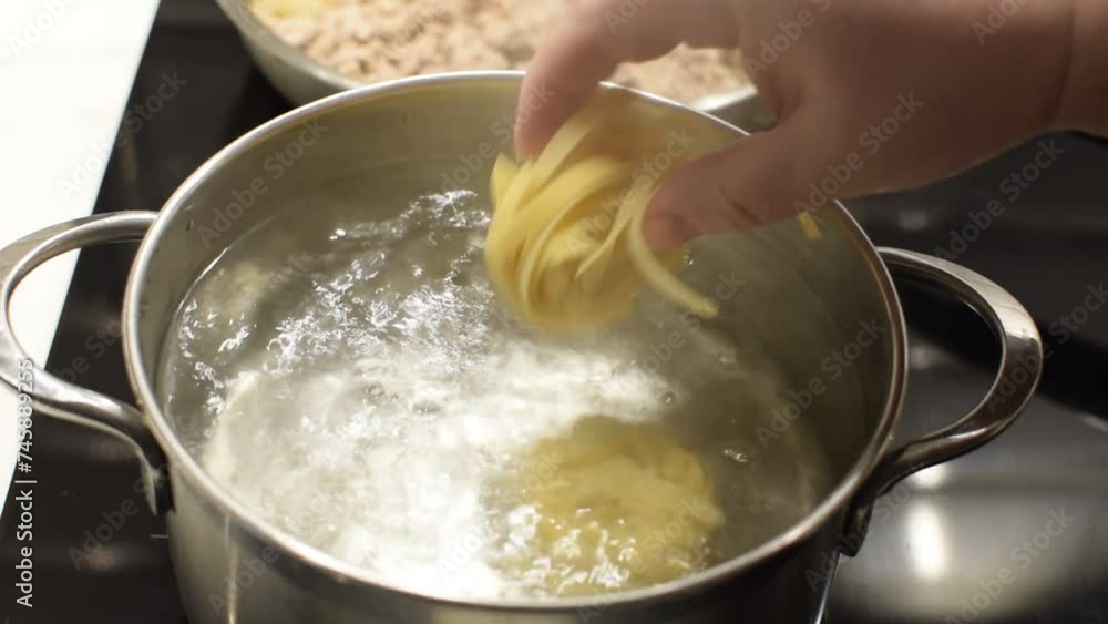 Nests of fettuccine pasta are thrown into boiling water. Nests of fettuccine pasta are thrown into boiling water.