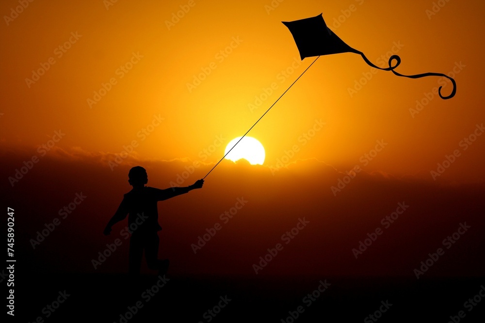The boy flies a kite under the sunset's glow, his silhouette outlined