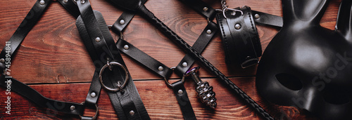 set of BDSM sex toys with handcuffs, whip flogger, butt anal plug for submission and domination on wooden background. Wide header cover for a horizontal banner for sex shop photo