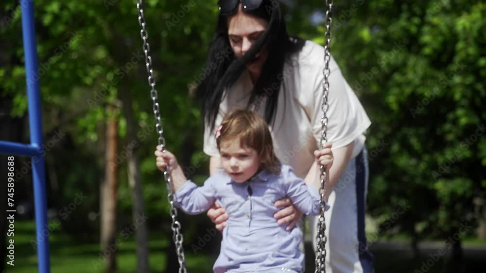Mom rides her daughter on a swing in the park Mom rides her daughter on a swing in the park