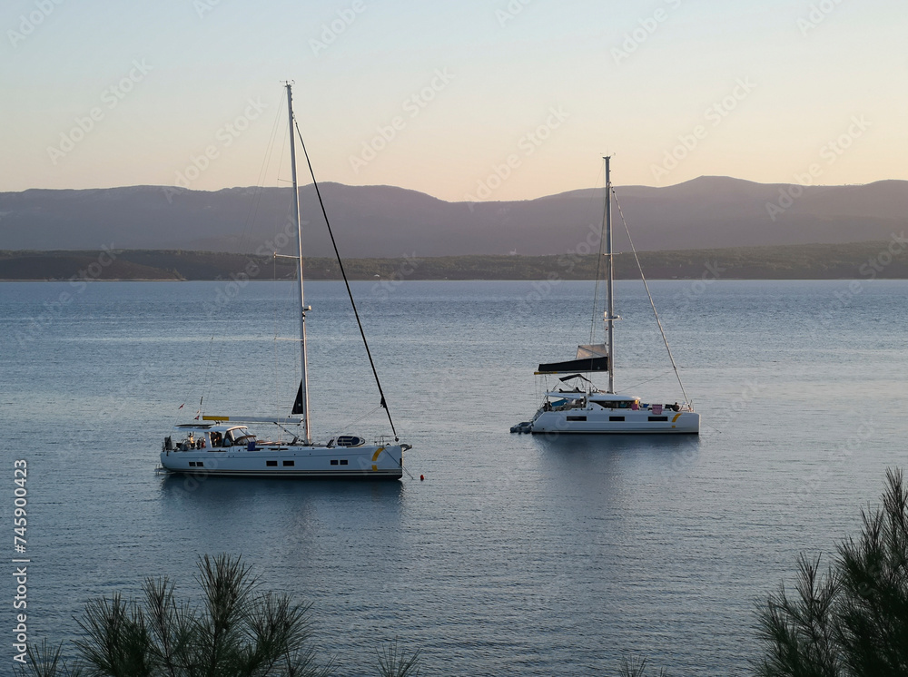 Two sailing boats are anchored in the bay at Zlatni Rat. Soft evening light shortly before sunset. The island of Hvar can be seen in the background.