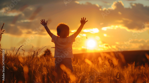 A Little Boy Raises His Hands Above the Sunset.