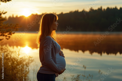 pregnant lady in profile, standing near a lake at dawn
