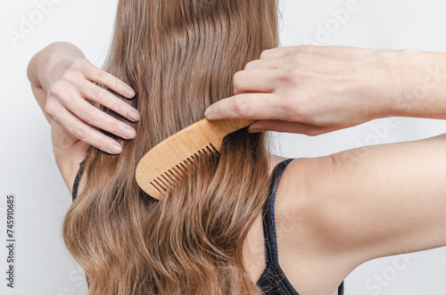 Wooden comb in a woman's hand combs shiny hair. Hair care and hygiene. Gray background.