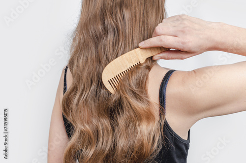 Wooden comb in a woman's hand combs shiny hair. Hair care and hygiene. Gray background.