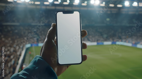 Man fan hands holding isolated smartphone device in soccer football crowed stadium game with blank empty white screen, sports betting concept photo