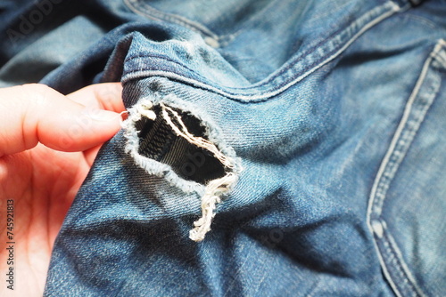 Hand touching ripped dark blue jeans cracked with hole at the crotch near back pocket Need to repair by sewing machine and stitching