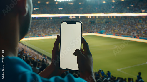 Man fan hands holding isolated smartphone device in soccer football crowed stadium game with blank empty white screen, sports betting concept photo