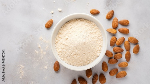 A bowl of almond flour surrounded by whole almonds on a light gray surface