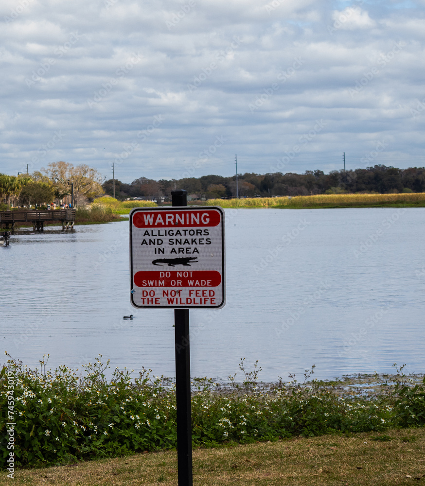 Alligator and snake warning sign beside lake with no swimming or feeding of wildlife
