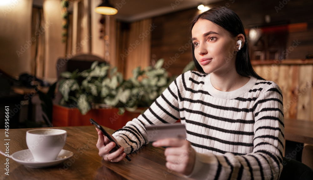 Woman paying with credit card online while making orders via the Internet sitting in cafe. Successful girl making transaction using mobile bank application. Woman paying with credit card online while making orders via the Internet sitting in cafe. Successful girl making transaction using mobile bank application.