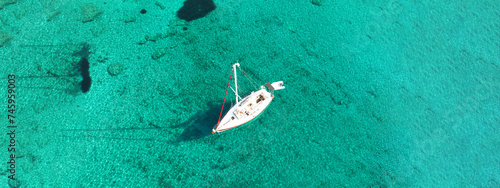 Aerial drone ultra wide photo of sail boat anchored in tropical exotic turquoise calm waters forming a blue lagoon