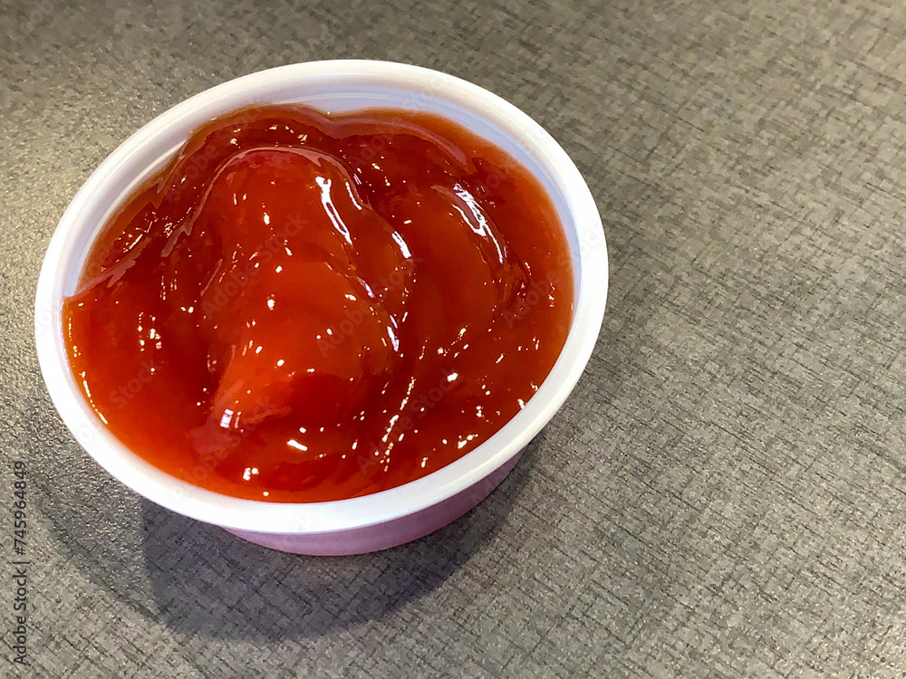Ketchup in a plastic ramekin on a gray background Ketchup in a plastic ramekin on a gray background