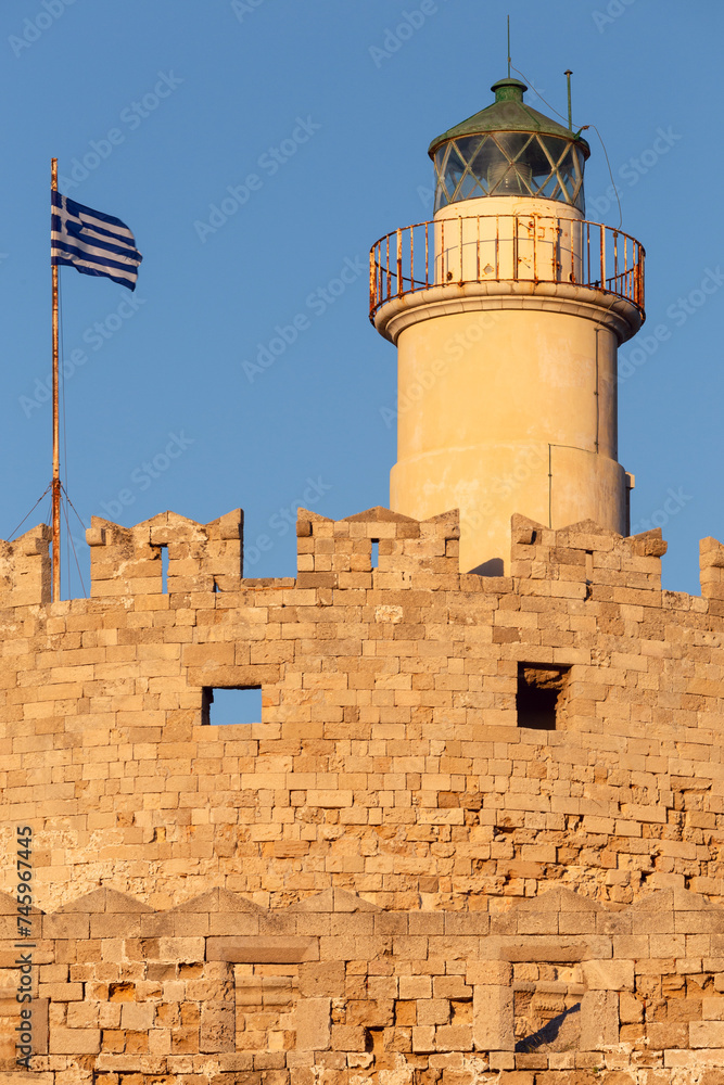 Old stone lighthouse illuminated by the sun at Fort St. Nicholas in Rhodes early in the morning.