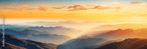 Panoramic view of a mountainous landscape enshrouded in the soft mist of early morning. Various shades of blue and grey layered effect. Light and shadow adds sense of tranquility to the scene.