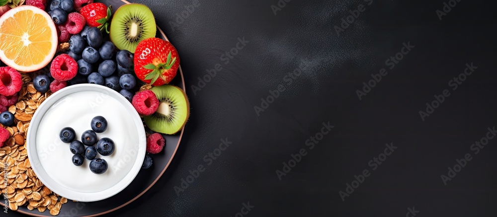 A plate containing a healthy breakfast spread of granola, Greek yogurt, various fruits, and blueberries laid out on a black background.