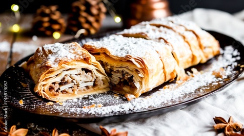  A scrumptious apple strudel dusted with powdered sugar, served on a plate with festive lighting in the background. Copy space.