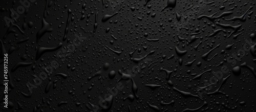 Numerous water drops are scattered across a black, plastic grainy abstract background. The drops reflect light, creating a striking contrast against the dark surface. photo