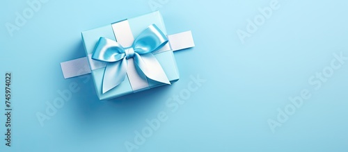 A luxurious blue gift box with a matching bow placed on a blue background. The high angle view showcases the monochrome close-up of this elegant item, perfect for occasions like Fathers Day,