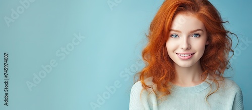 A close-up portrait of a young  beautiful woman with ginger red hair smiling at the camera. She is holding a blank sign against a blue pastel background  creating a cheerful and engaging image.