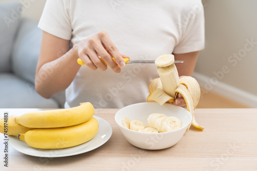 Healthy of tropical fruit in summer concept, woman cutting banana slices on table, preparing smoothie, salad in kitchen room, eating fresh ripe banana to get energy, vitamin from natural organic food.