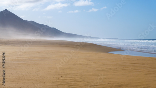 Menschenleerer Strand von Cofete mit Dunst und Wellen und Sonnenschein