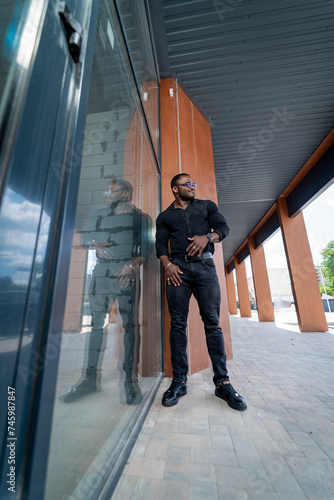 Handsome black man is standing near the glass wall and looking at the camera., handsome black man is standing near the glass wall and looking at the camera. © Vadim