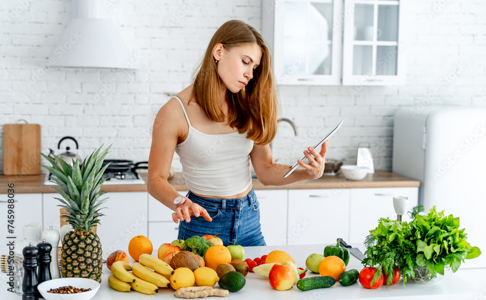 Young woman standing in the kitchen with tablet computer and using mobile phone for shopping online, Young woman standing in the kitchen with tablet computer and using mobile phone for shopping online