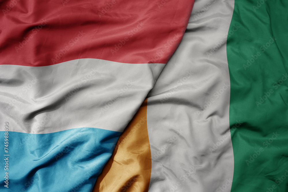 Obraz premium big waving national colorful flag of cote divoire and national flag of luxembourg .