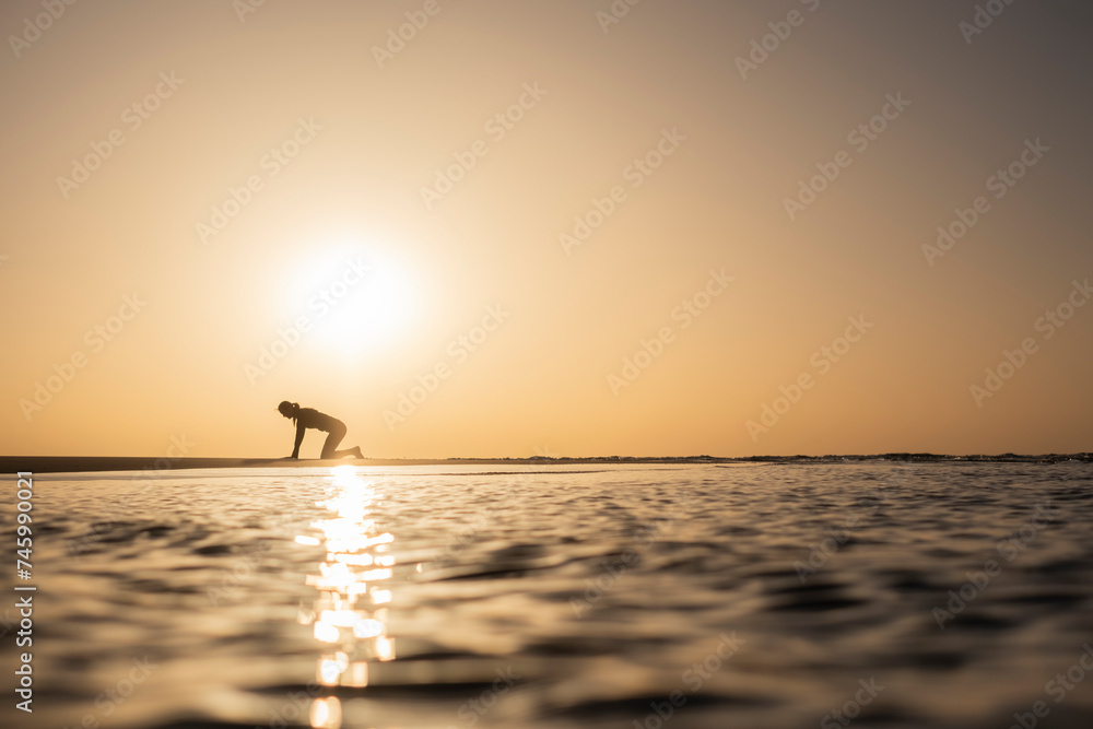 Mujer practicando yoga a la salida del sol en la orilla del Océano
