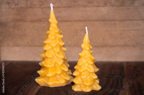 Two bees wax candles shaped like pine trees, wood background 