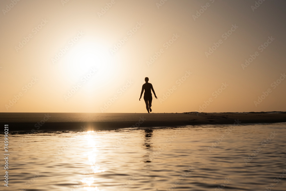 Mujer saltando en la orilla del Océano, salida del sol