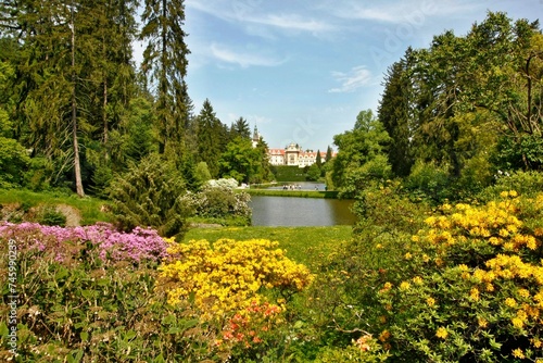 Castle park with blooming bushes and a pond. View across the water to Průhonice Castle in the Czech Republic