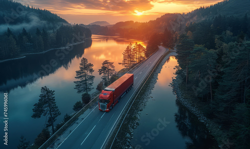 Red truck driving on the asphalt road through the forest in the mountains in the light of sunset