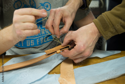 Cropped image of two men sewing a leather belt