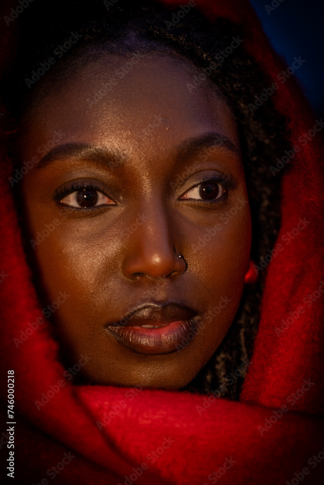 In this intimate close-up, the subject's face is partially shrouded in shadow, illuminated intriguingly by ambient light that highlights the contours of her face. The crimson fabric of her wrap In this intimate close-up, the subject's face is partially shrouded in shadow, illuminated intriguingly by ambient light that highlights the contours of her face. The crimson fabric of her wrap