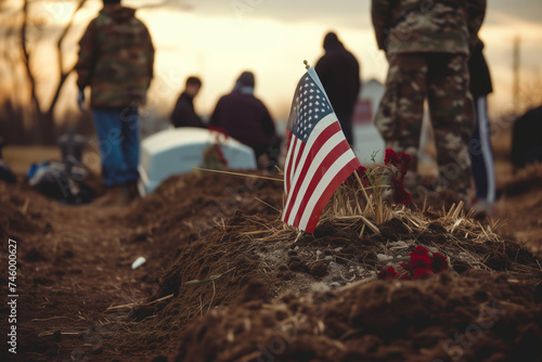 American flag by fresh grave at military funeral, with soldiers and mourners in the background. photo